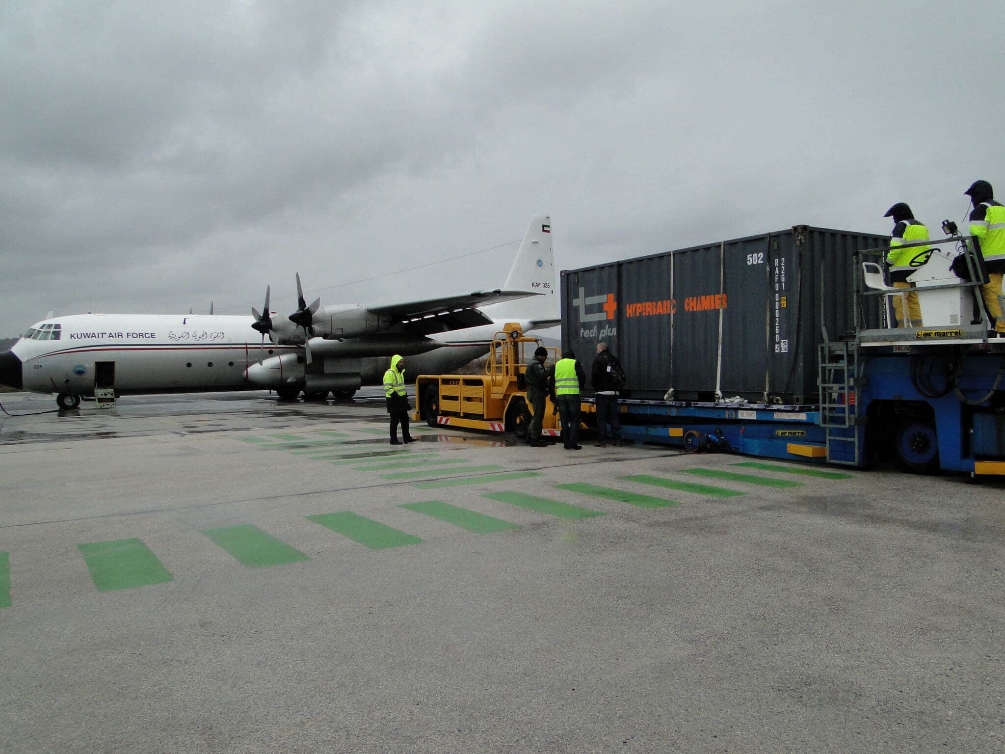 Caisson hyperbare conteneurisé Tech Plus sur une plateforme de chargement, près d'un avion de transport militaire