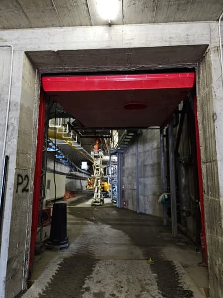Porte sectionnelle rouge ouverte dans une galerie de tunnel en béton, nacelle en arrière-plan