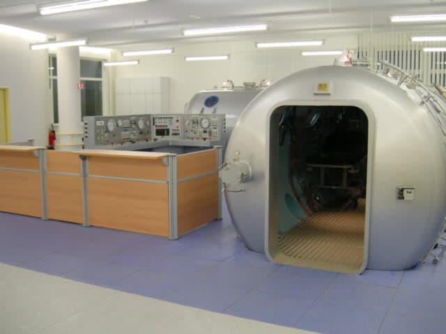 Caisson hyperbare multiplace hospitalier, porte ouverte, à côté de son pupitre de commande